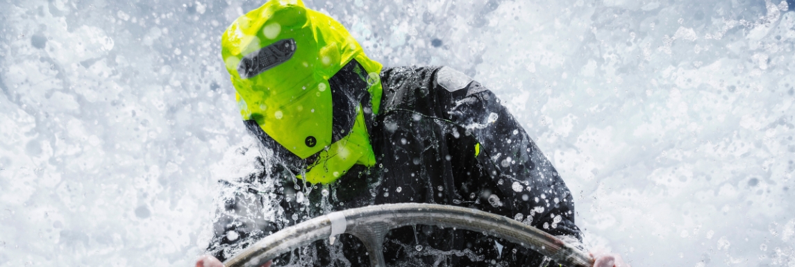 Homme à la barre en tenue bateau avec capuche sous une intempérie